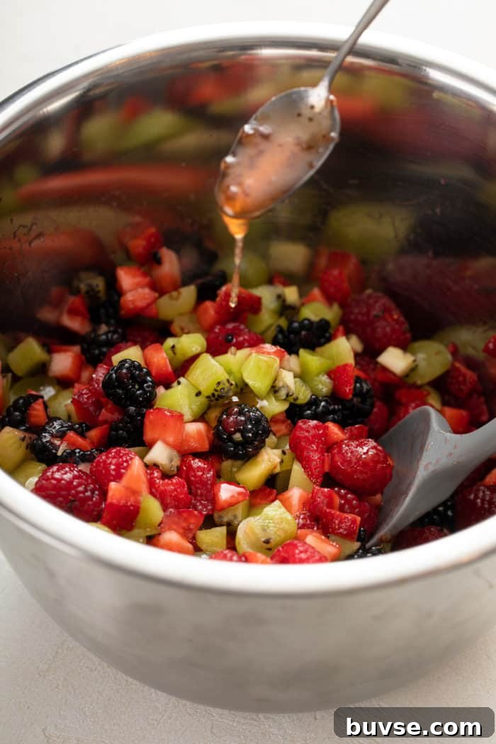 Fresh Fruit Salsa Recipe with Lime and Cilantro 7 Spoon drizzling dressing over diced fresh fruit in a metal bowl.