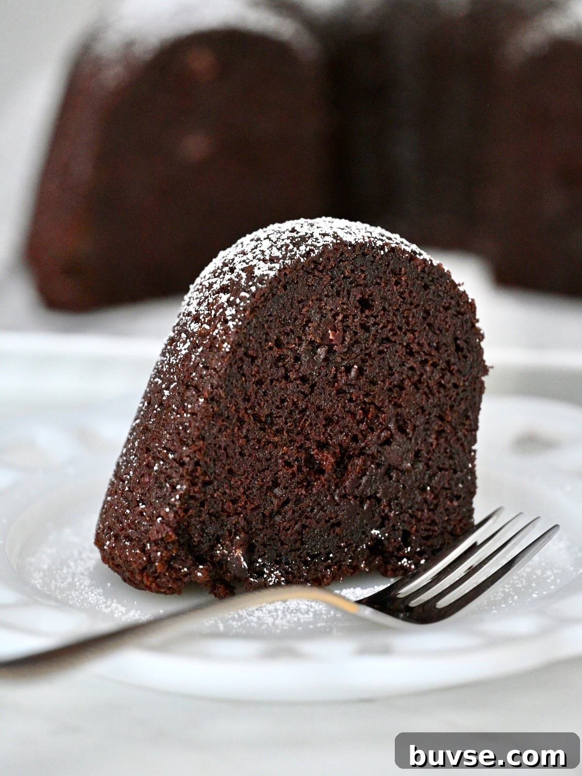 Moist Double Chocolate Chip Bundt Cake 3 Single slice of moist chocolate bundt cake with chocolate chips and powdered sugar on a plate with a fork.