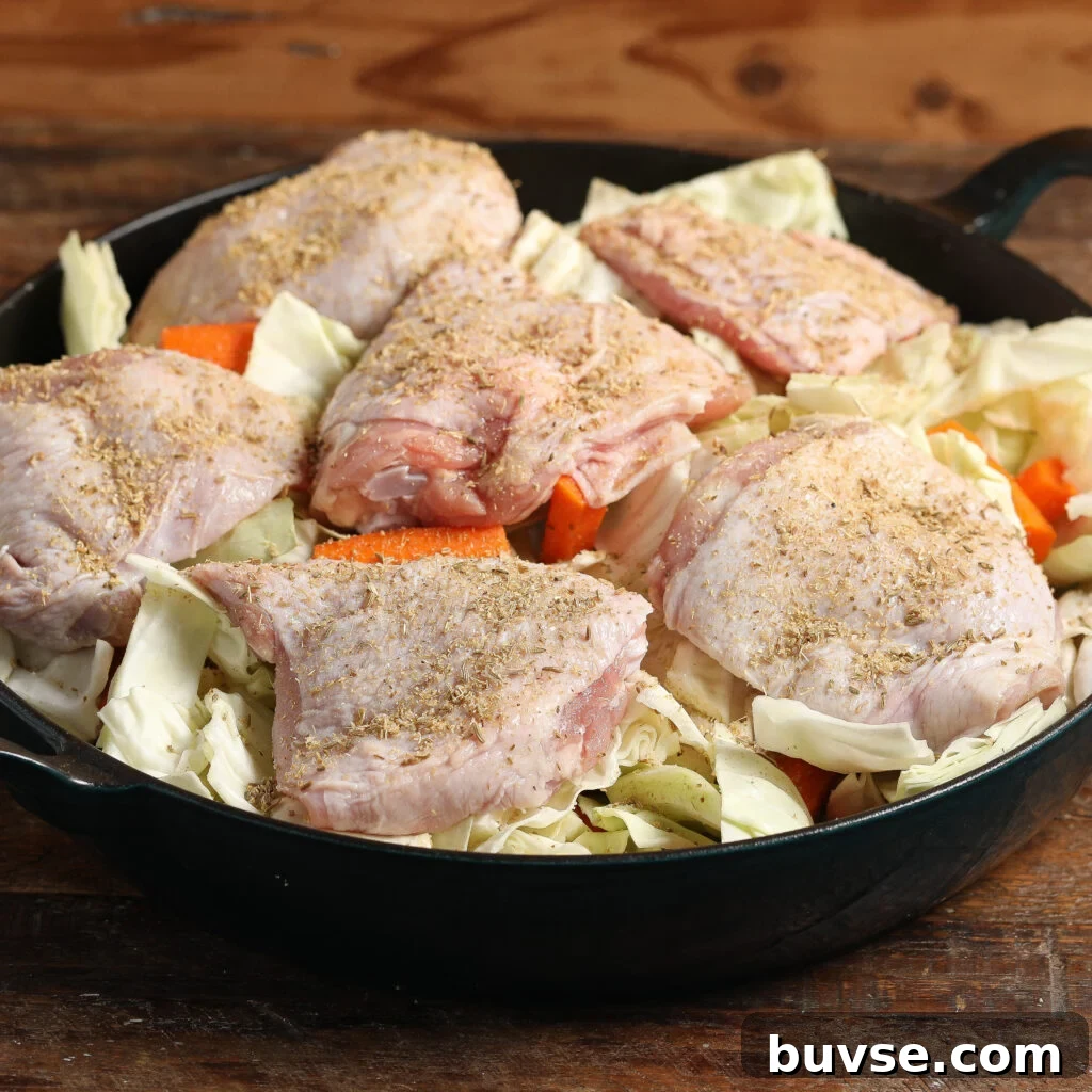 Roasted Chicken with Cabbage and Carrots 3 Raw seasoned chicken thighs nestled over chopped cabbage and carrots in a black skillet, ready for roasting.
