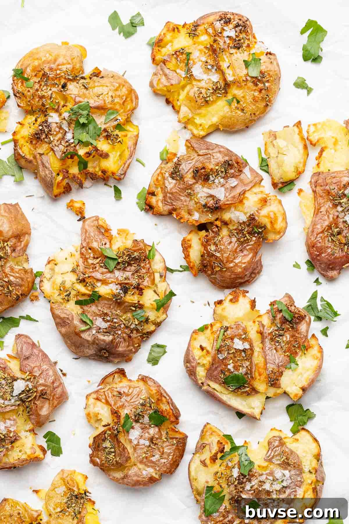 smashed potatoes garnished with parsley on sheet of parchment paper.