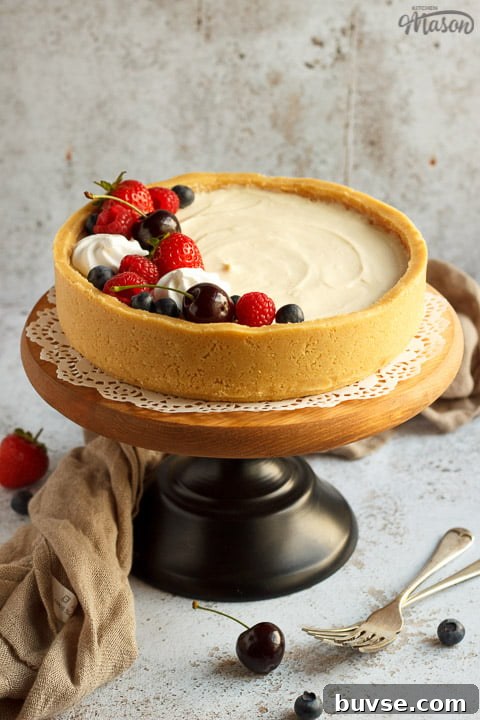 No bake vanilla cheesecake on a cake stand topped with mixed berries, surrounded by a light brown napkin and two forks