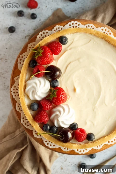 No bake vanilla cheesecake on a cake stand topped with mixed berries, surrounded by a light brown napkin and two forks