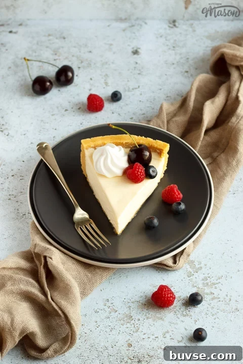 A slice of no bake vanilla cheesecake on a grey plate with a fork, topped with mixed berries, surrounded by a light brown napkin