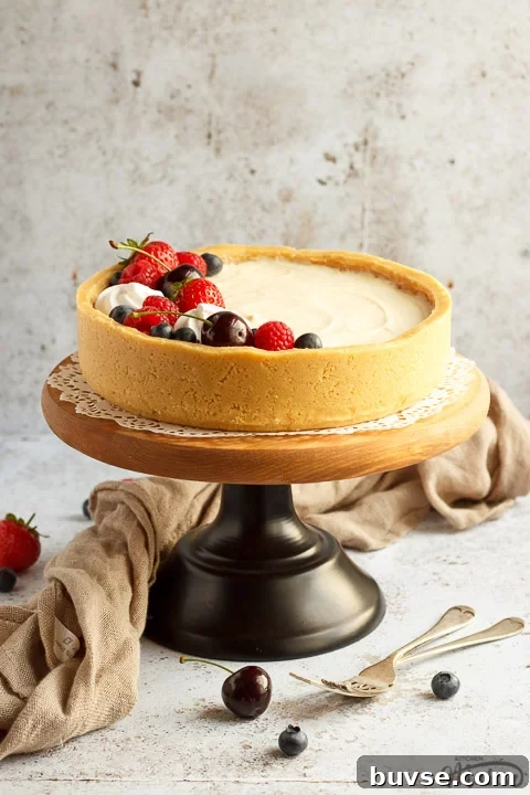 No bake vanilla cheesecake on a cake stand topped with mixed berries, surrounded by a light brown napkin and two forks