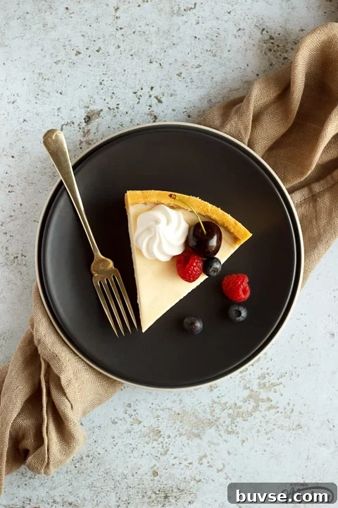 A slice of no bake vanilla cheesecake on a grey plate with a fork, topped with mixed berries, surrounded by a light brown napkin