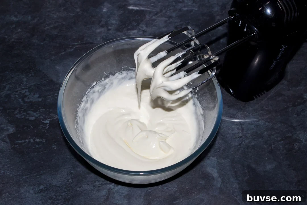 Cream and icing sugar whipped to soft peaks in a glass bowl with an electric hand whisk