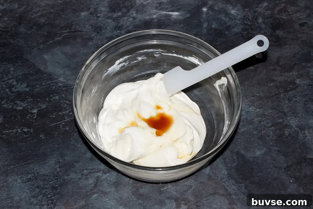 Cream cheese, sugar, soured cream and vanilla extract in a glass bowl with a spatula