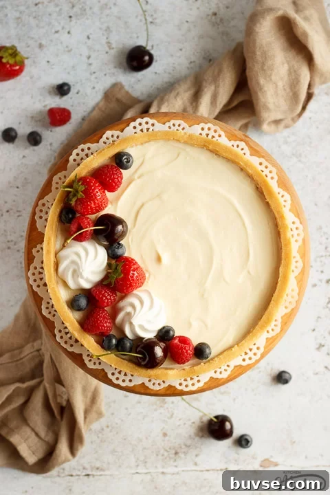 A no bake vanilla cheesecake on a cake stand topped with mixed berries surrounded by a light brown napkin