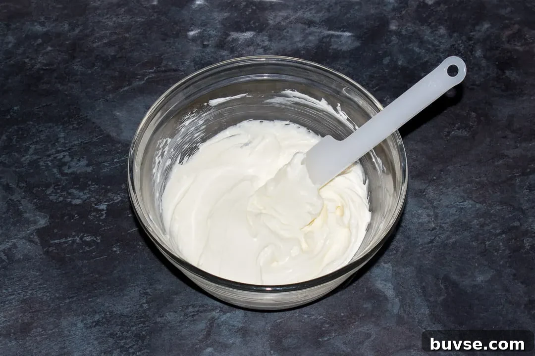 Softened cream cheese and sugar in a glass bowl with a spatula.
