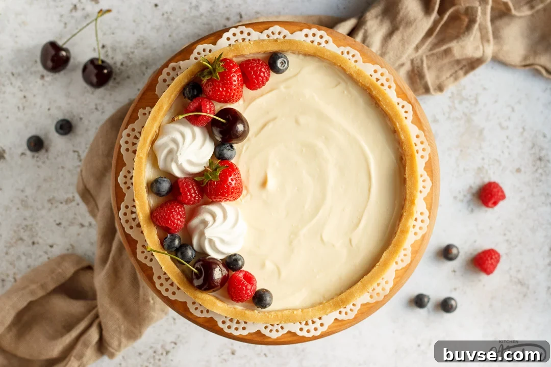 A no bake vanilla cheesecake on a cake stand topped with mixed berries surrounded by a light brown napkin.
