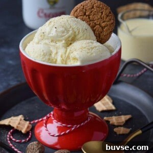 Three scoops of eggnog ice cream in a red cup with a gingersnap on top.