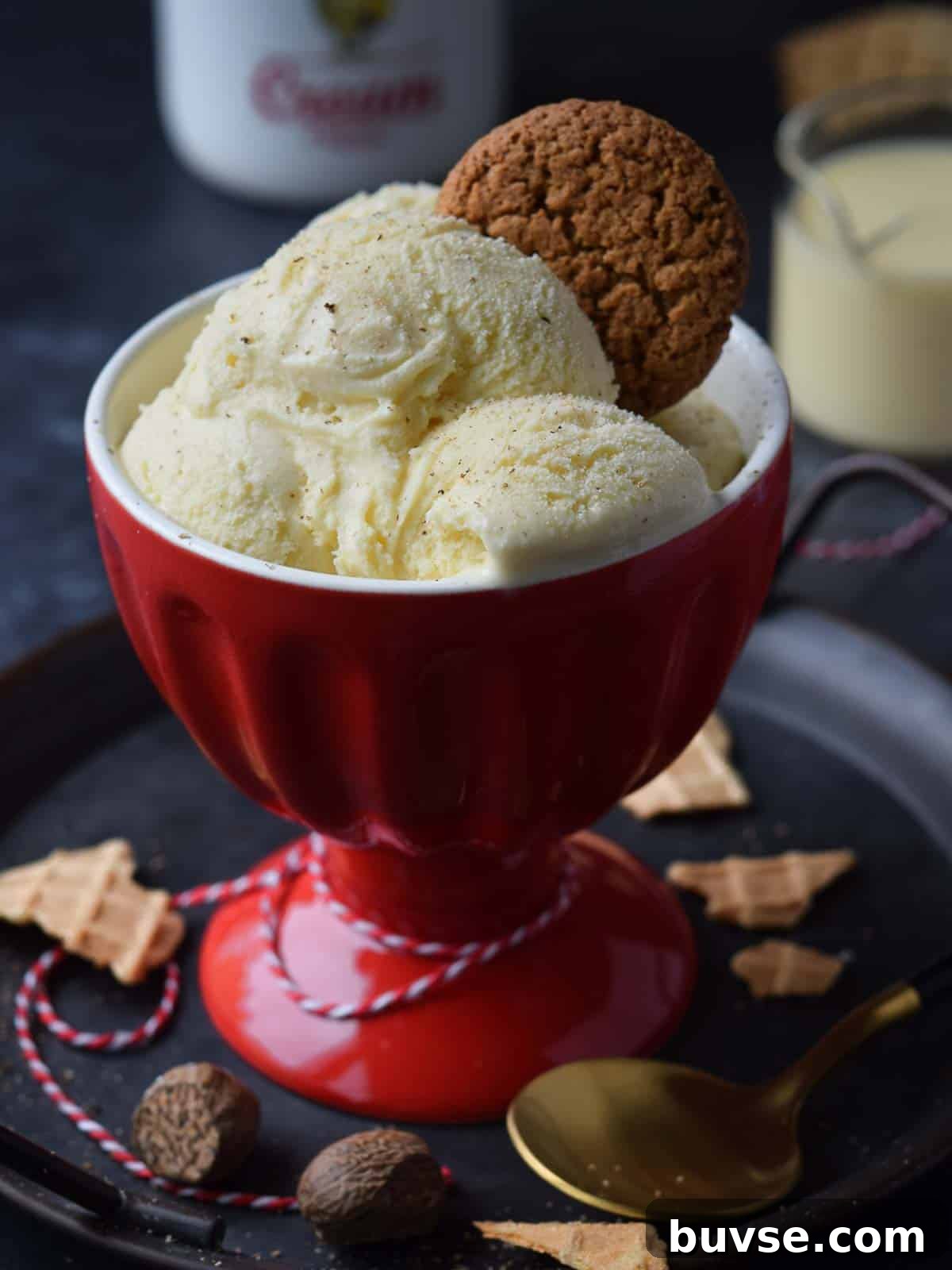 Three scoops of eggnog ice cream in a red cup with a gingersnap on top.
