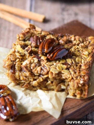 Baked pecan pie oatmeal on a wood slab with cinnamon sticks in the background.