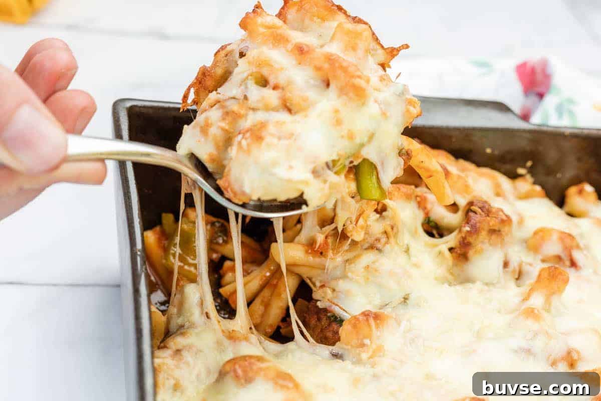 A hand lifts a serving of meatball casserole from a rectangular baking dish, showing melted cheese stretching.