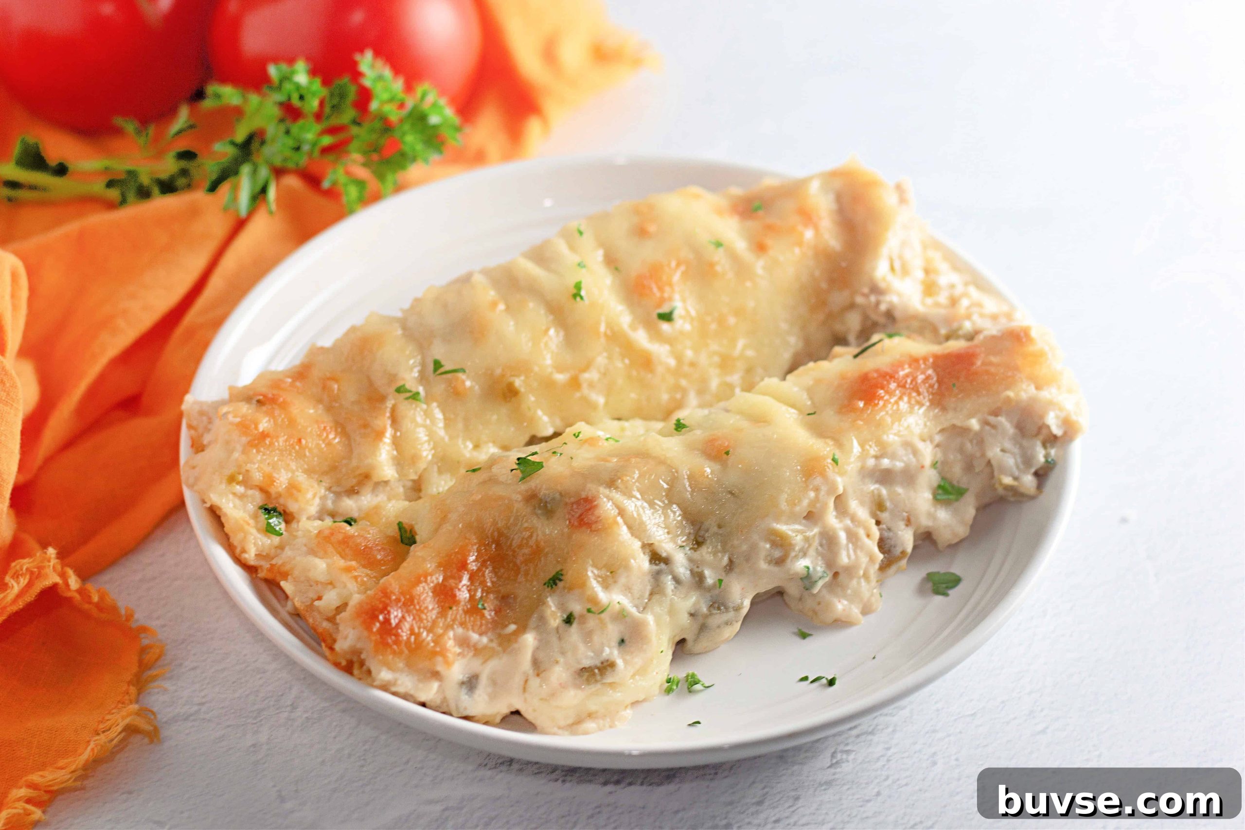 Two White Chicken Enchiladas filled with creamy sauce and topped with melted cheese, served on a white plate with a garnish of chopped parsley.