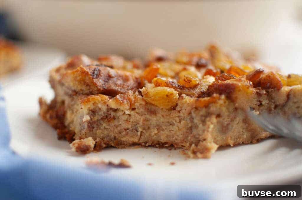 A close-up of a slice of Cinnamon Roll Casserole topped with golden raisins on a white plate.