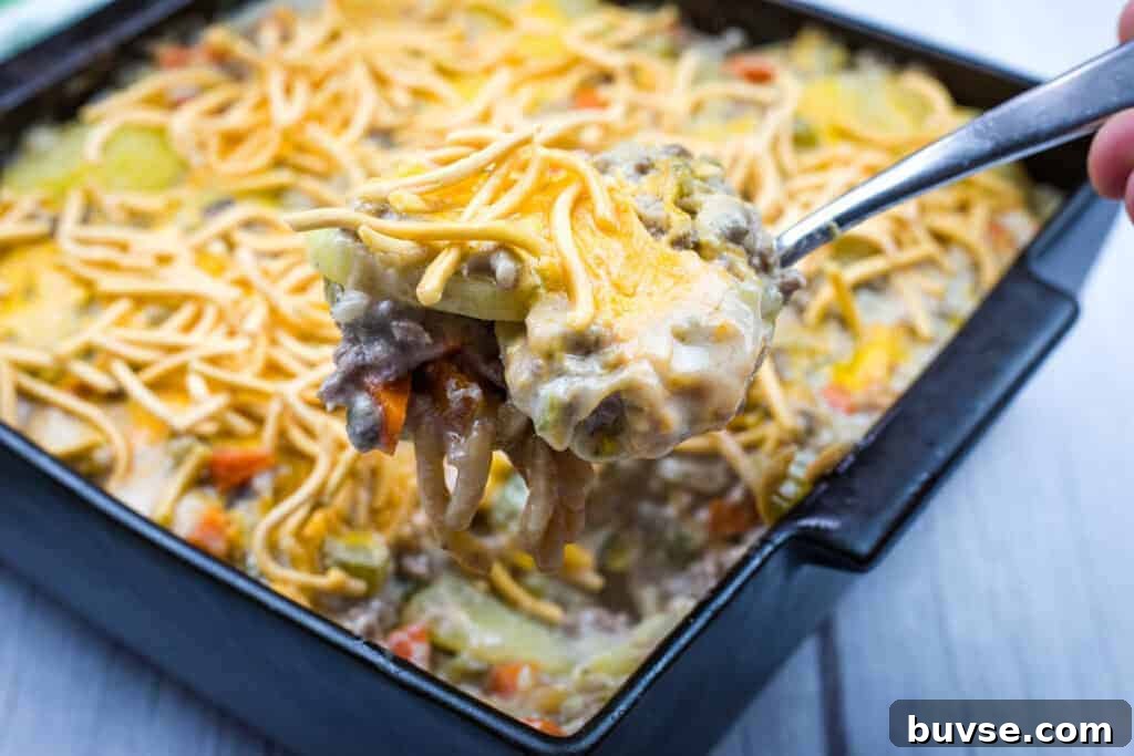 A close-up of a spoonful of Church Potluck Hot Dish with Chow Mein Noodles taken from a black square baking dish.