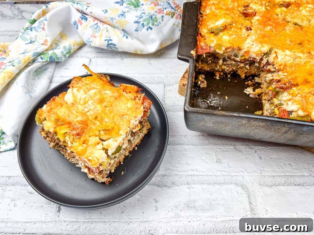 A slice of John Wayne casserole on a black plate beside a baking dish of the same casserole.