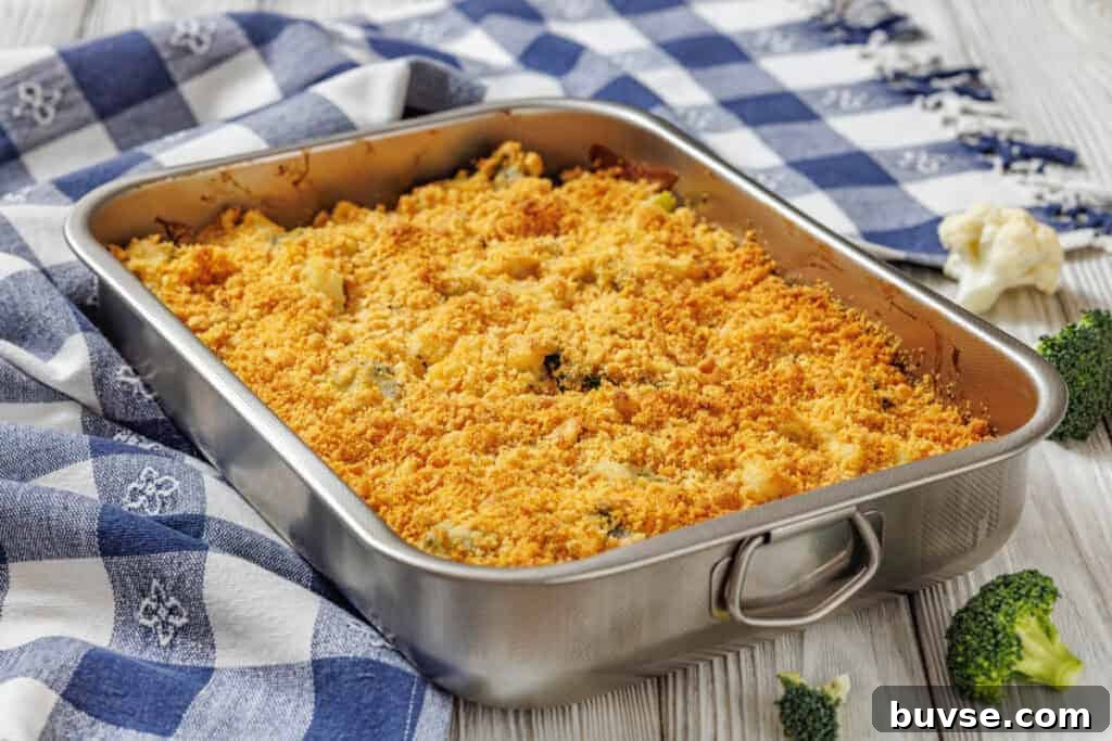 Cheesy Broccoli & Cauliflower Casserole with Crispy Bacon in a metal dish on a blue and white checkered cloth, with broccoli and cauliflower nearby.