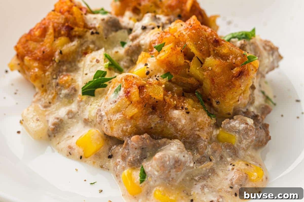 A serving of Slow Cooker Cowboy Casserole topped with crispy tater tots and black pepper on a white plate.