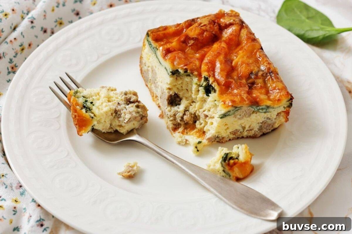 A slice of Sausage, Spinach, and egg casserole on a white plate, with a fork holding a bite-sized piece.