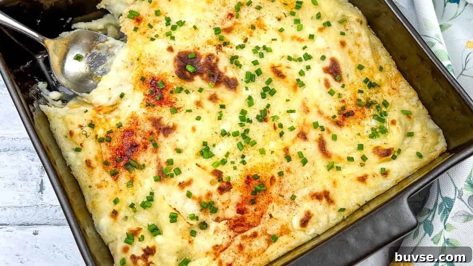 A close-up of Grandma's Mashed Potato Casserole with a serving spoon in the dish.