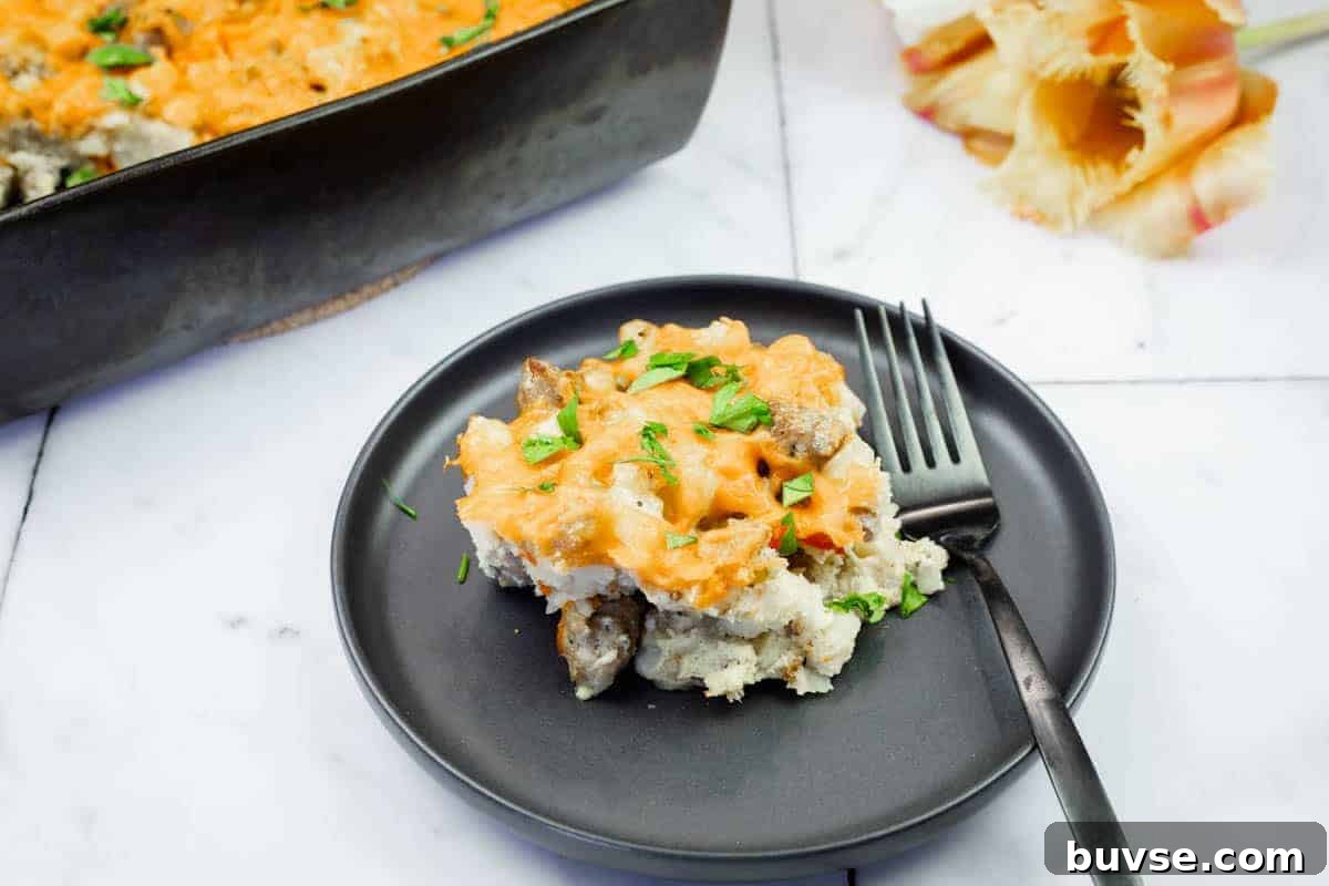 A serving of Sausage-Hash Brown Breakfast Casserole on a black plate with a fork, next to a baking dish and pasta shells on a marble surface.