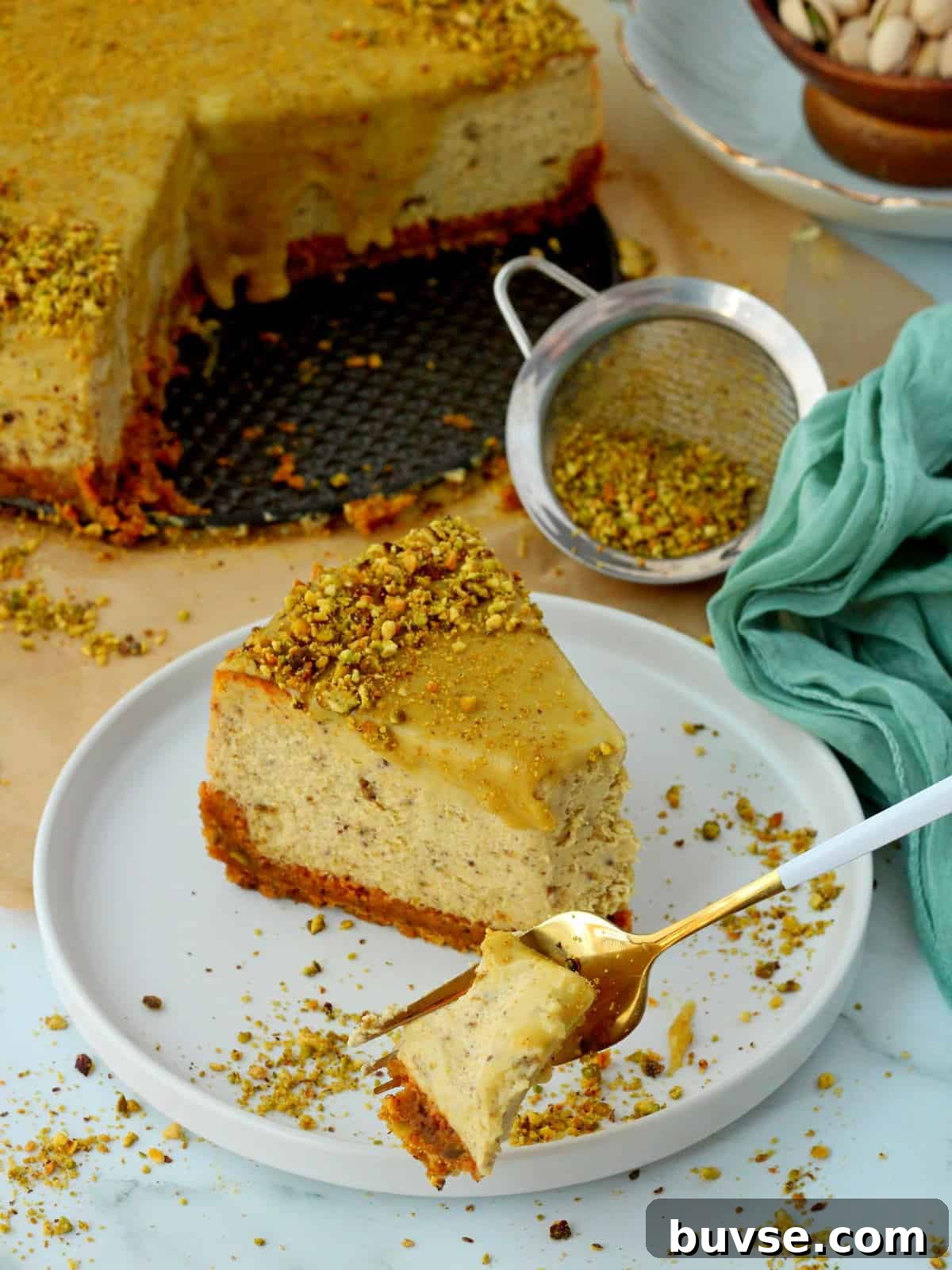 Slice of pistachio cheesecake on white plate. White fork is digging into the first bite.