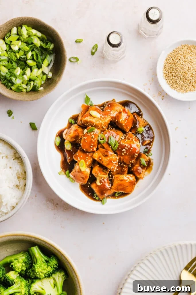 Teriyaki salmon bites in a serving dish garnished with green onion and sesame seeds.