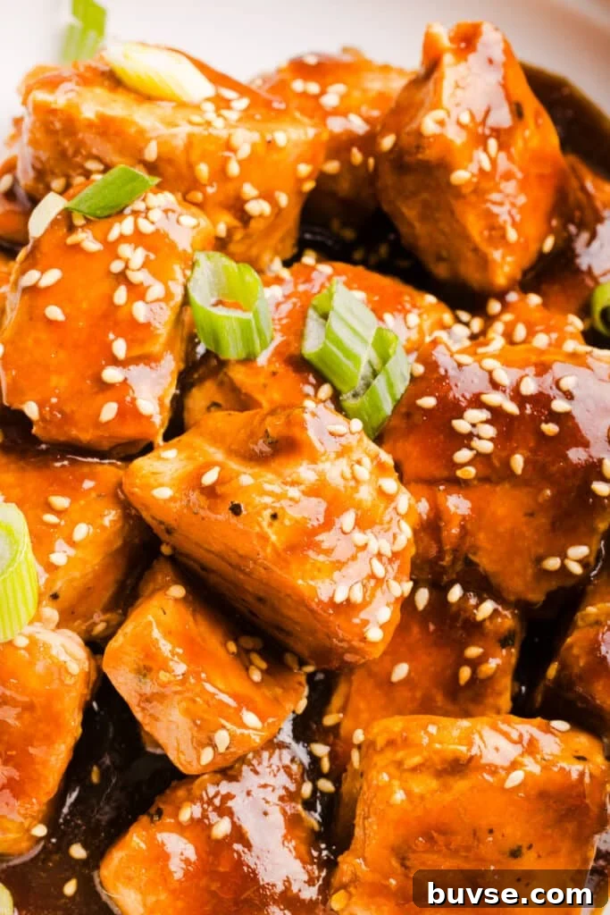 A tight shot of teriyaki salmon bites garnished with sesame seeds and green onions.