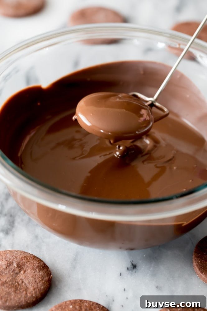 A chocolate cookie that's just been dipped in a bowl of melted chocolate and lifted out for the excess chocolate to drip off