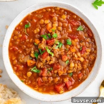Bowl of vegan lentil soup garnished with parsley, with bread on the side.
