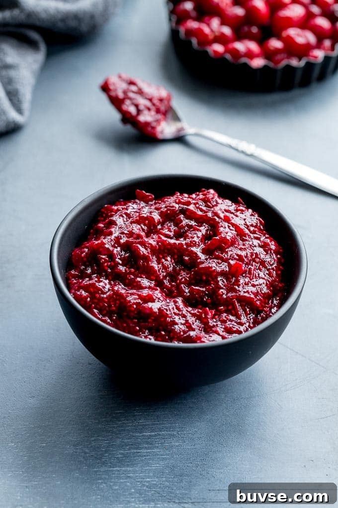 Healthy Cranberry Sauce in a black bowl on a blue surface with cranberries in the background.