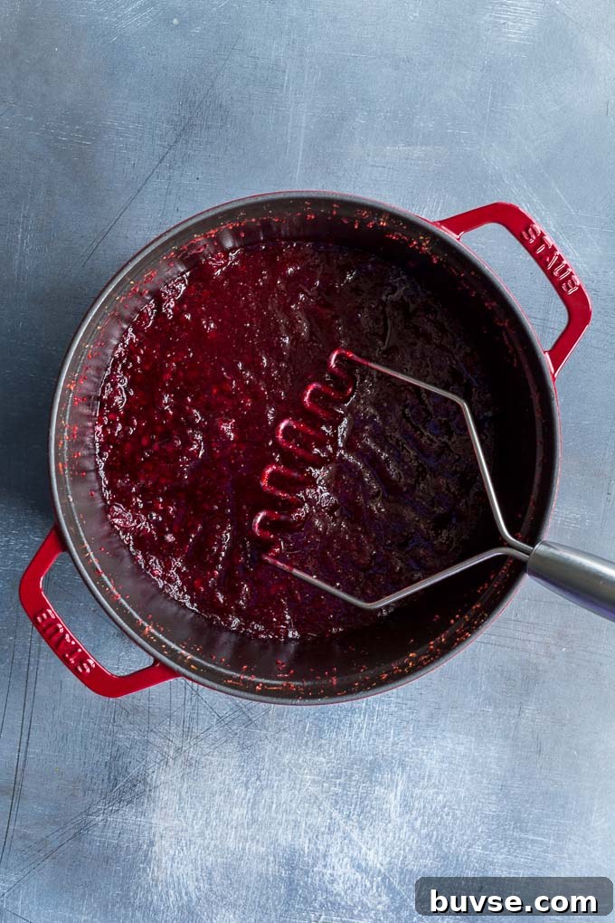 Overhead view of softened fruit for the cranberry sauce being mashed in a large pot.