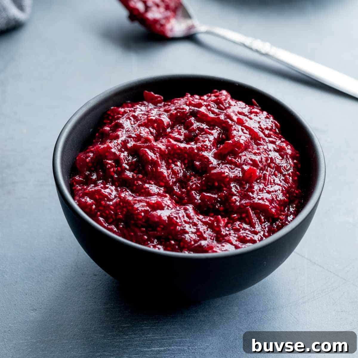 Angled view of healthy cranberry sauce in a small black bowl with a spoon in the background.