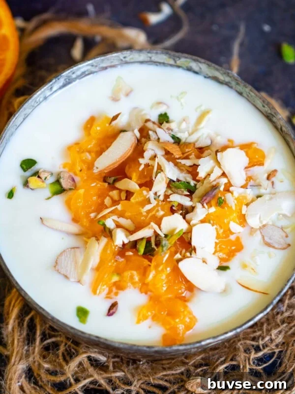 A bowl of orange kheer topped with orange segments and chopped nuts.