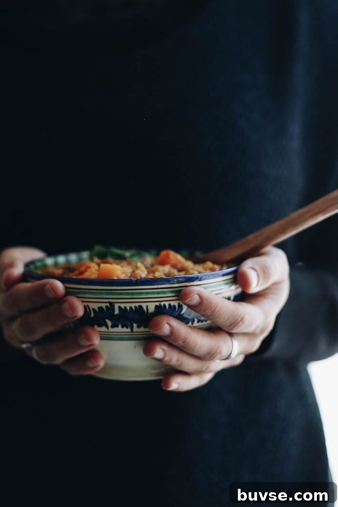 Hands holding a dal recipe in a decorative bowl.