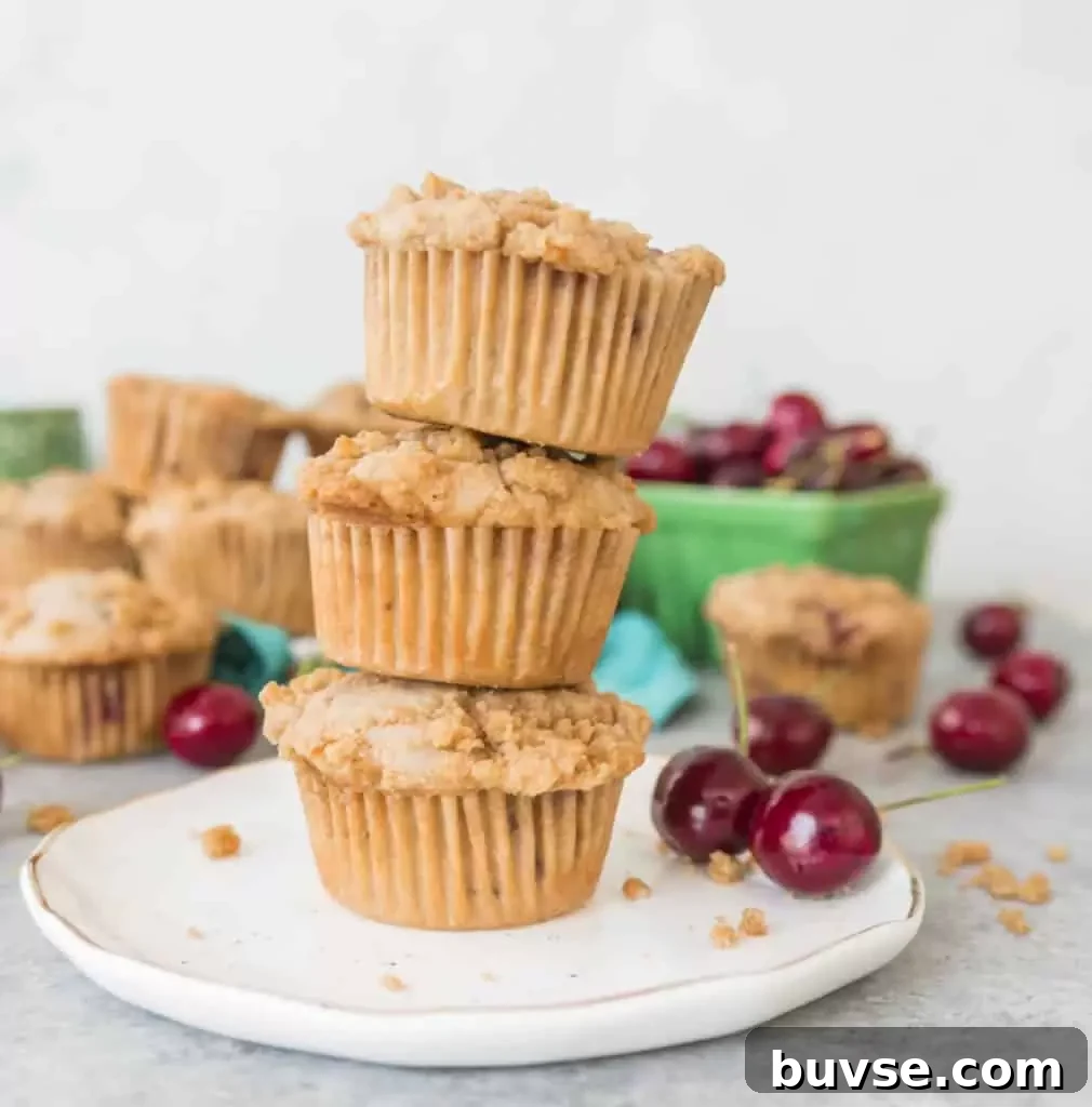 Stack of cherry cobbler muffins on a plate in front of a basket of cherries