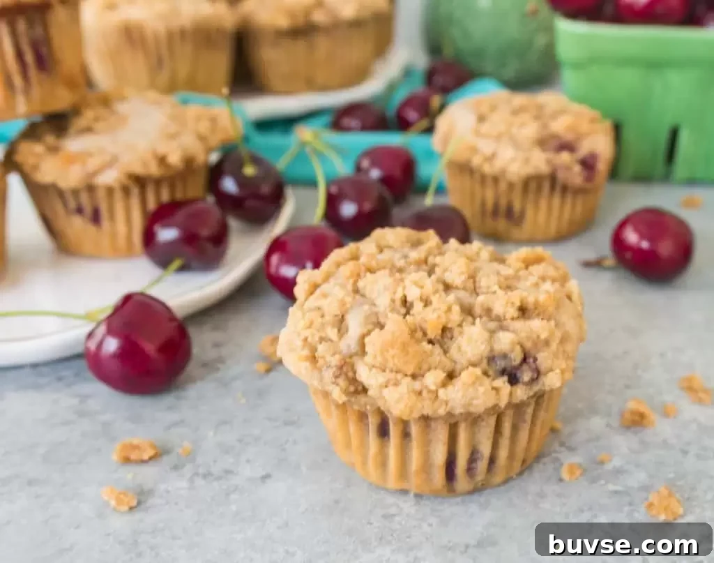 Muffin sitting in front of more cherry cobbler muffins with cherries and crumb topping scattered around it