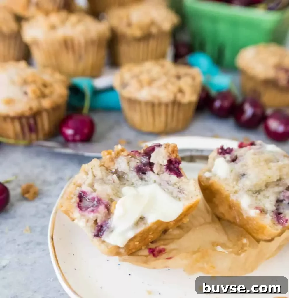 Muffin split open and topped with melting butter sitting in front of more cherry cobbler muffins