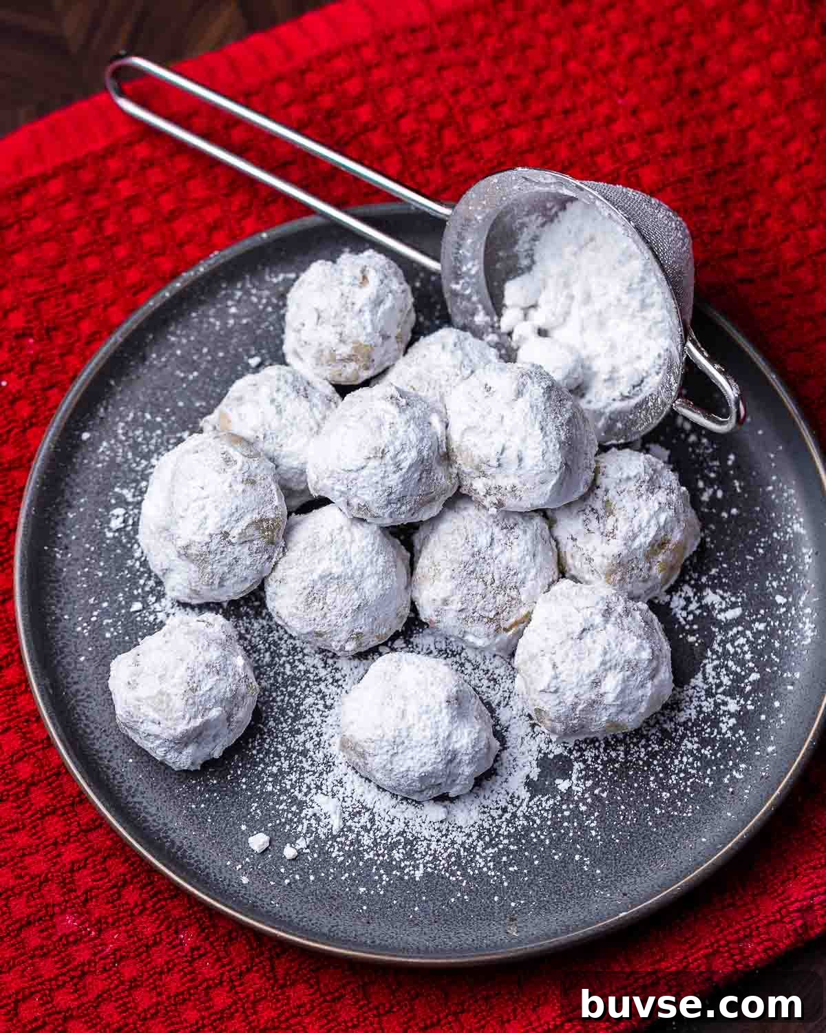 Plate of walnut snowball cookies on top of red towel.