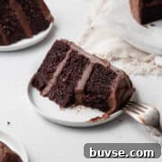 A bitten slice of gluten free chocolate cake with chocolate frosting on a small white plate.