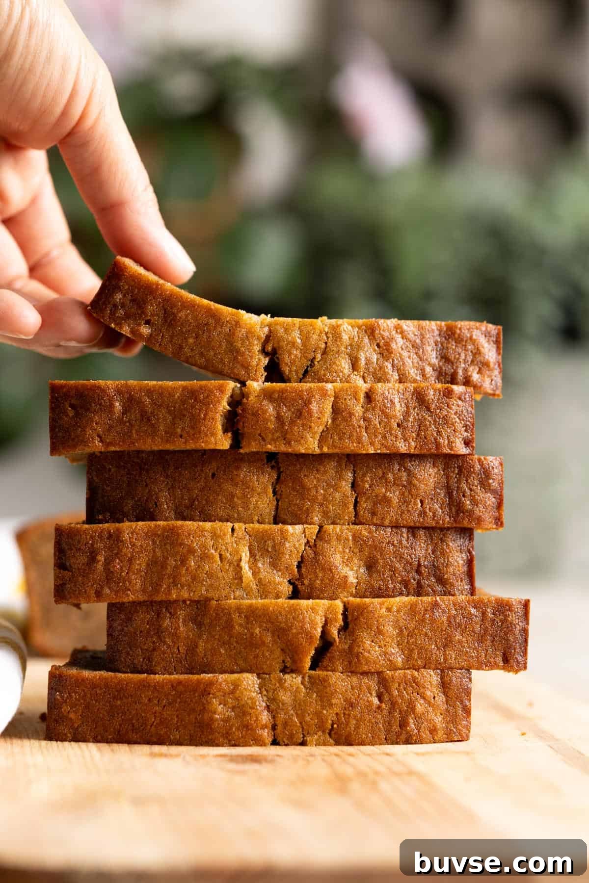 One-Bowl Brown Butter Mochi Banana Bread Recipe 11 A stack of mochi banana slice with a hand lifting up the top slice.