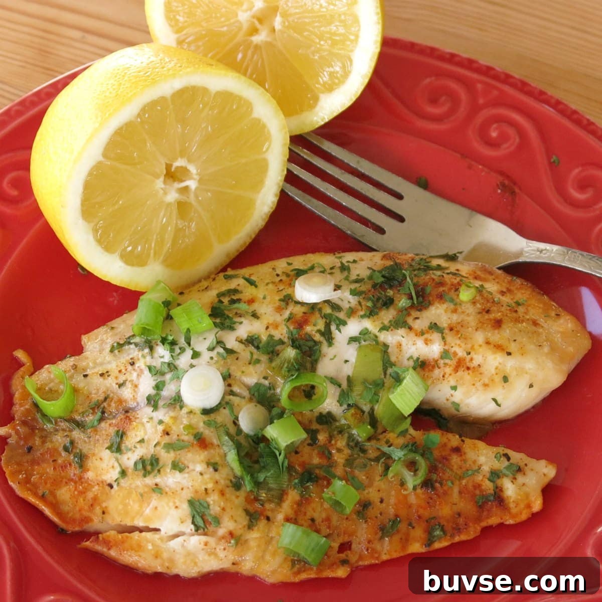 Baked lemon pepper tilapia on plate with a lemon halves and a fork.