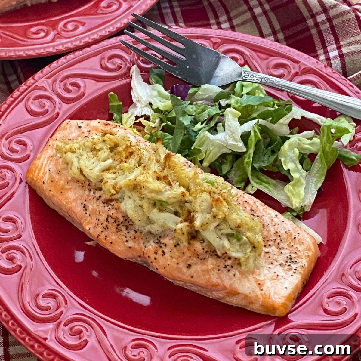 Crab stuffed salmon on a red plate with a salad and fork next to it.