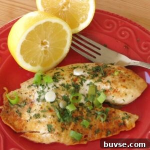 Baked lemon pepper tilapia on plate with a lemon half and fork.