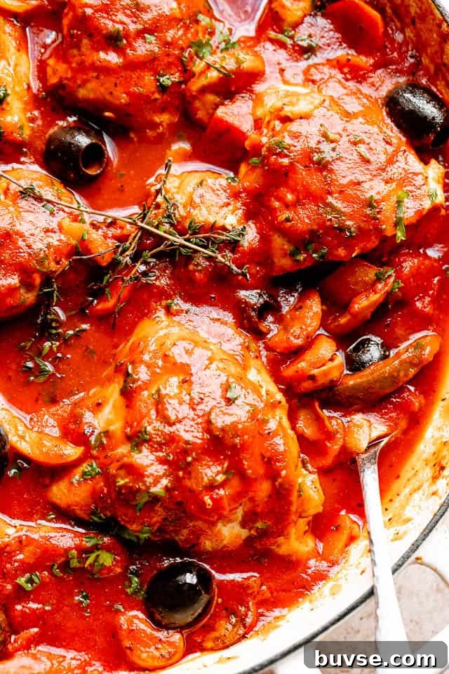 Chicken pieces topped with fresh herbs and black olives in a large pot ready to be served.