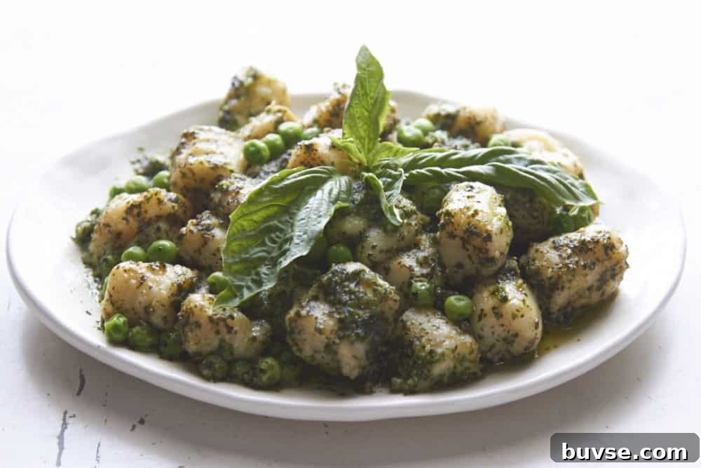 Gnocchi with pesto and peas topped with fresh basil on a white plate.