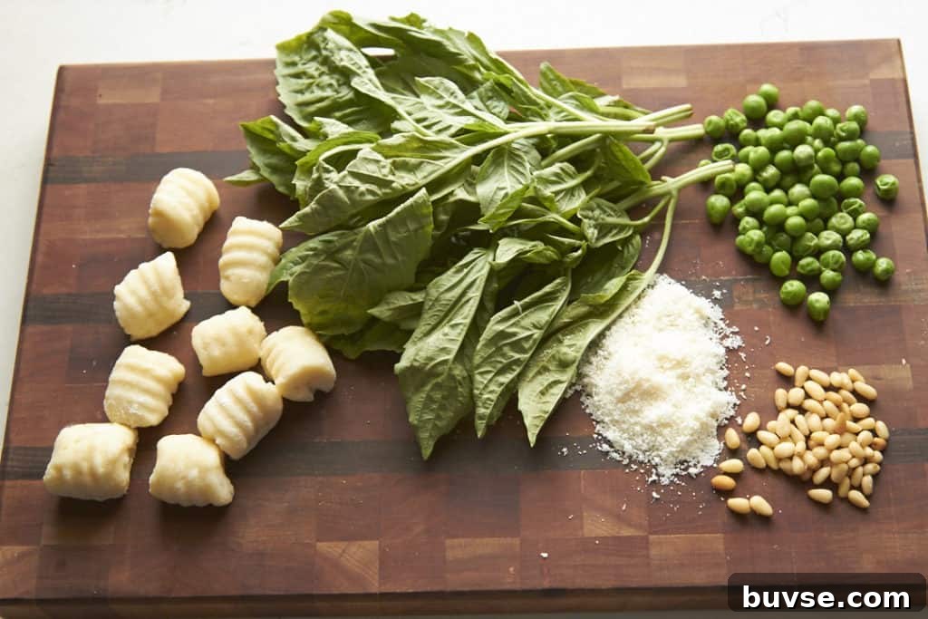 Gnocchi, fresh basil, peas, parmesan cheese, and pine nuts on a wooden cutting board.