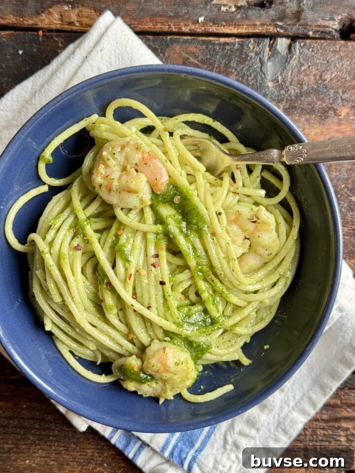 A bowl of shrimp and pesto pasta with a fork